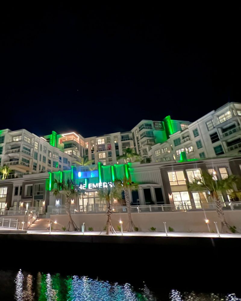 Views of The Emerson On Rocky Point apartments from the bay at night with green lights illuminating the building.